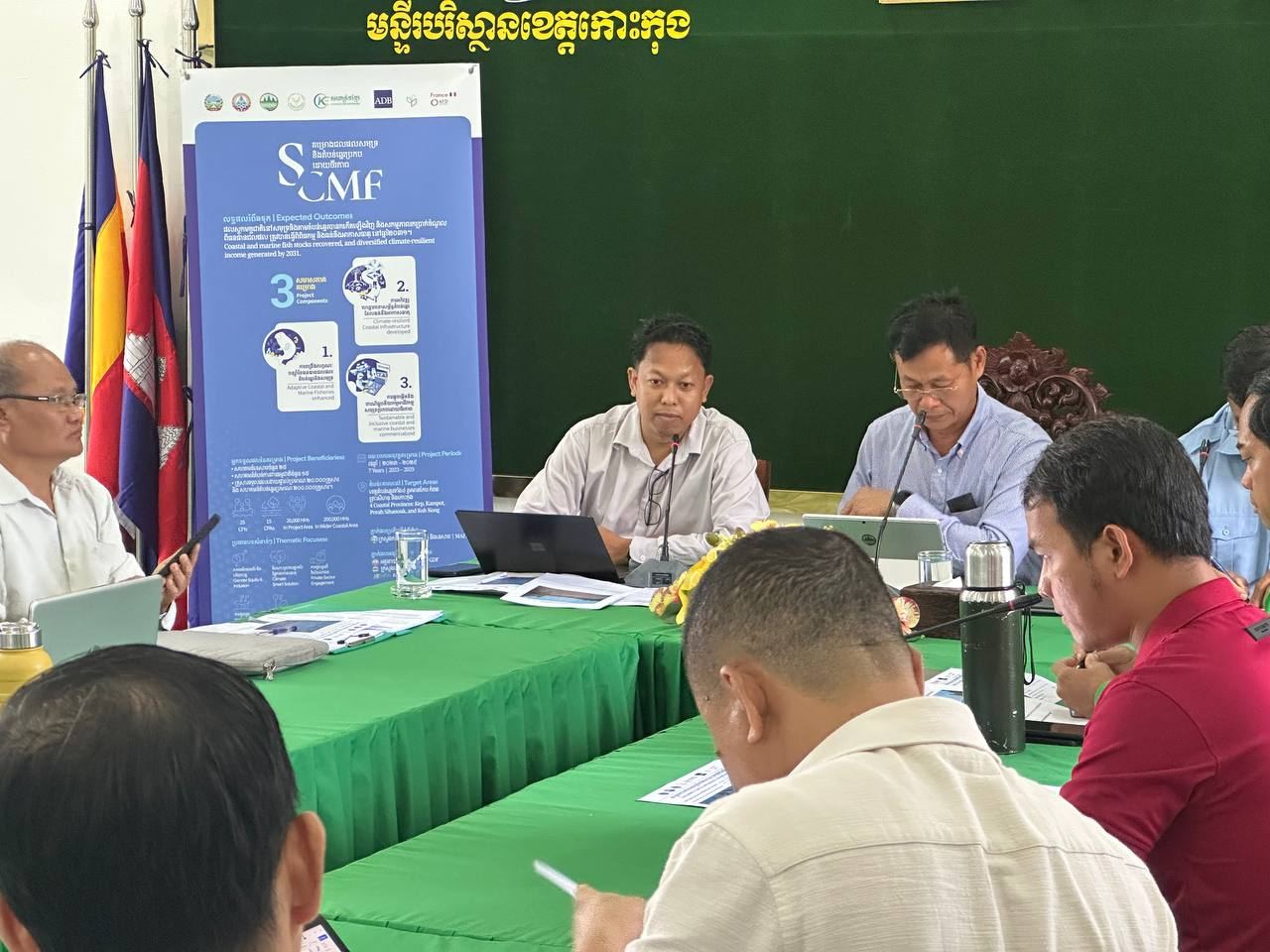 Officials and the Bright Life team around a meeting table beside an SCMF project banner