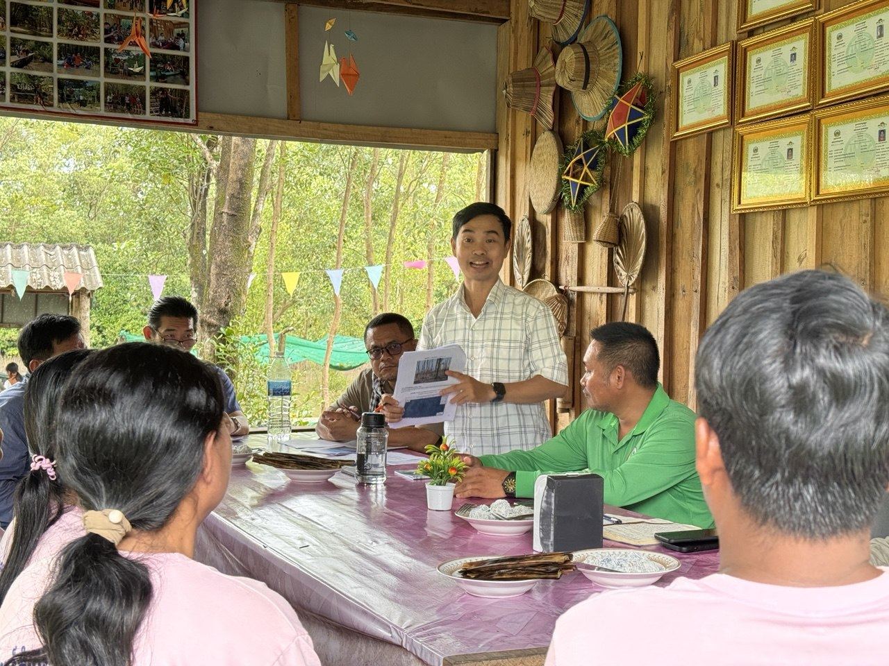 Team leader Eam Dyna holding printed material while speaking with villagers at a long table