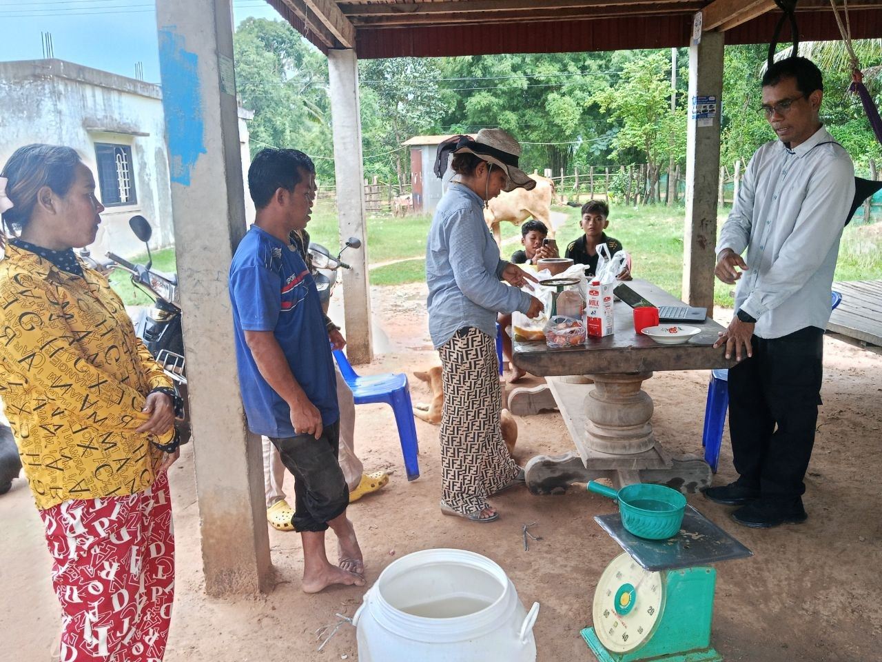 Households gather around a table and scale while weighing ingredients for organic fertiliser